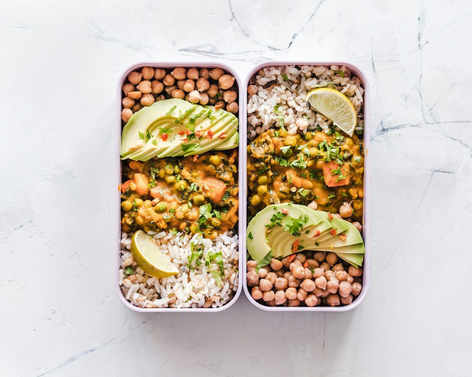 Due box già pronti con riso, ceci, verdure, avocado e limone, visti dall’alto